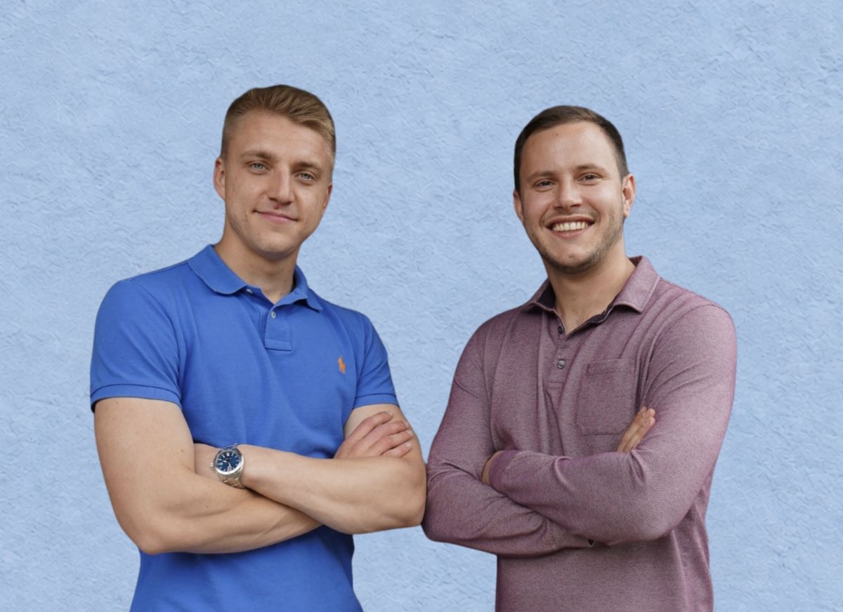 Die Geschäftsführer Leon Meurisse und Werner Dilzer stehen mit verschränkten Armen vor einer hellblauen Wand und lächeln.