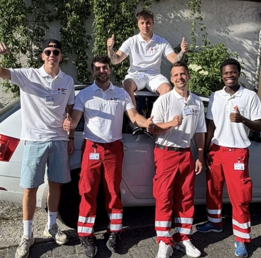 Sechs Fundraiser in Rotkreuz-Kleidung stehen gut gelaunt vor einem Auto, einige zeigen den Daumen nach oben.