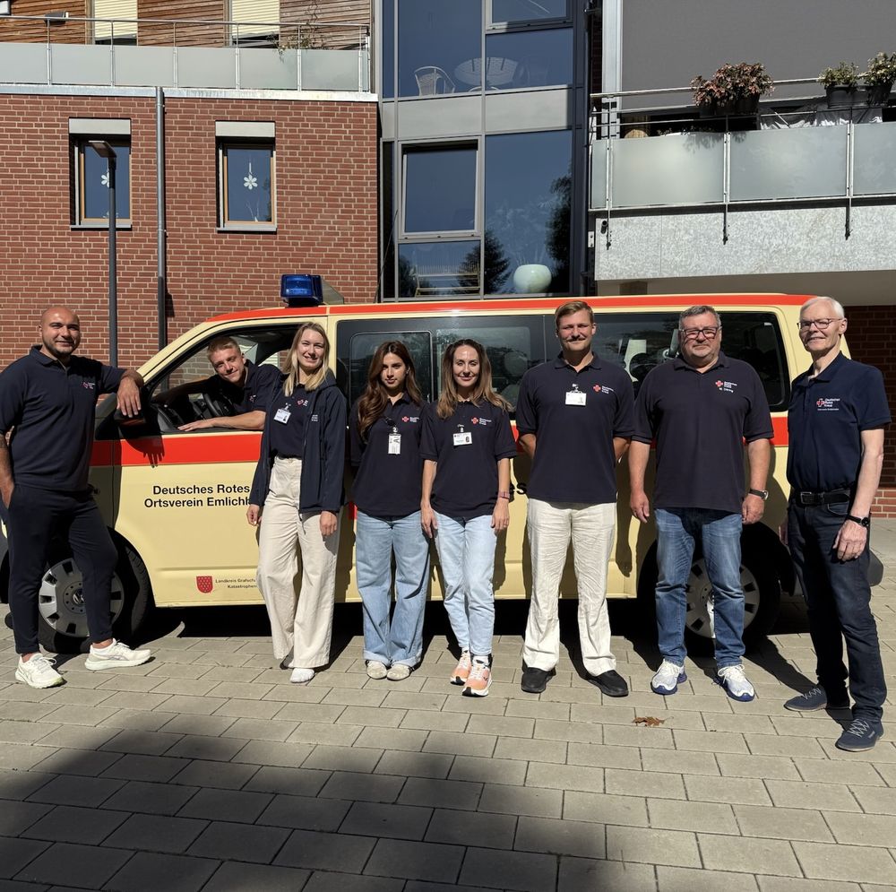 Gruppenfoto von neun Personen in dunkelblauen Poloshirts vor einem Fahrzeug des Deutschen Roten Kreuzes.