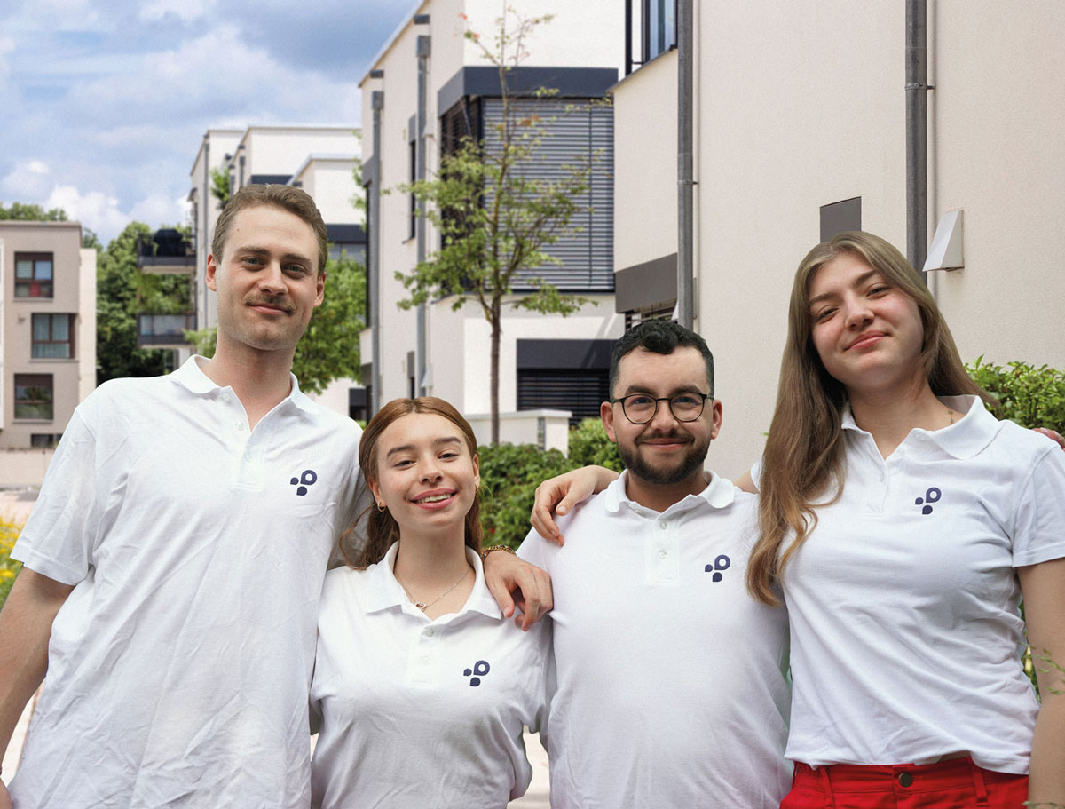 Vier junge Menschen stehen in einem Wohngebiet und lächeln. Sie sind Teil des Fundraising-Teams von mdp und tragen Merch-Kleidung.